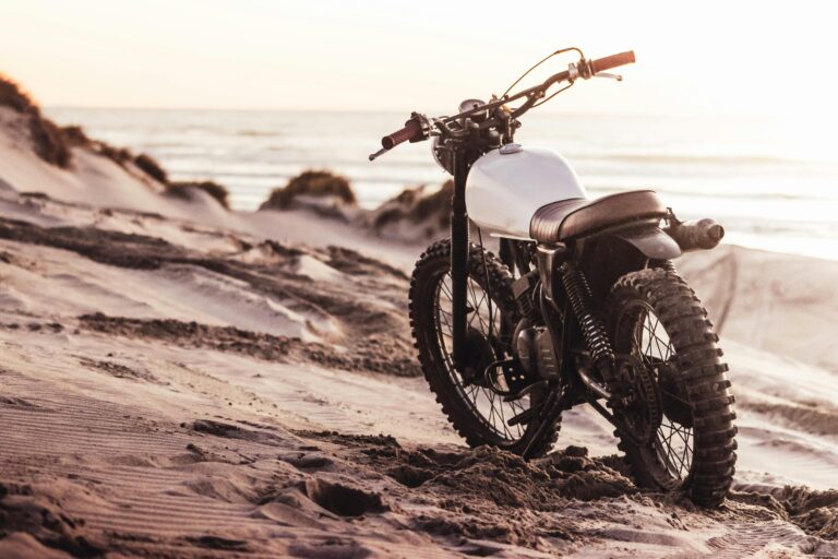A vintage dirt bike parked on a sandy beach with a beautiful sunset in the background, conveying adventure and freedom.